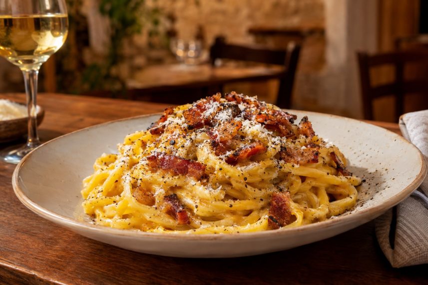 Un piatto di pasta alla carbonara con guanciale e pepe su un tavolo di trattoria.